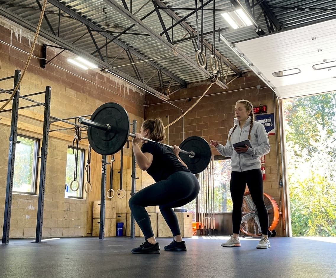 Doctor of Physical Therapy coaching an athlete through a barbell front squat as part of strength-based running rehab inside The Athlete's Physical Therapist performance gym, South Windsor CT